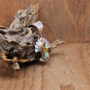 May include: A silver pendant with a turquoise and brown stone set in a silver design. The pendant has a silver bail with the word "CWM" engraved on it.