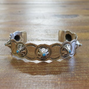 May include: A silver cuff bracelet with a decorative design featuring turquoise stones. The bracelet has a rounded shape and is made of polished silver.