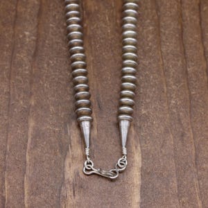 May include: A silver necklace with a beaded design. The necklace is made of small, round beads that are strung together in a spiral pattern. The necklace has a clasp at the back.