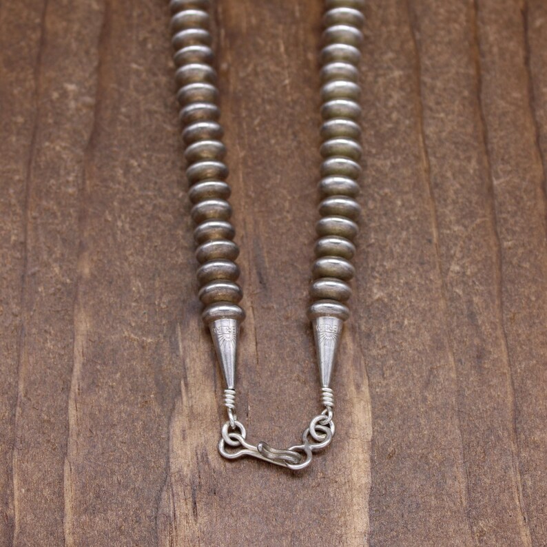 May include: A silver necklace with a beaded design. The necklace is made of small, round beads that are strung together in a spiral pattern. The necklace has a clasp at the back.
