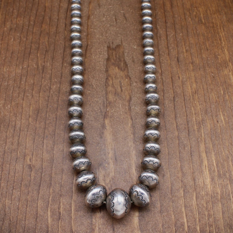 Puede incluir: Un collar de plata con una gran cuenta redonda en el centro y cuentas redondas m&aacute;s peque&ntilde;as a cada lado. Las cuentas est&aacute;n todas decoradas con dise&ntilde;os intrincados.