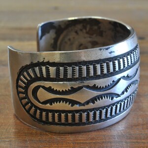 K&ouml;nnte beinhalten: Ein silbernes Armreif mit geometrischem Muster. Das Armband ist aus Sterlingsilber und hat eine geh&auml;mmerte Oberfl&auml;che.