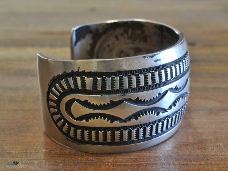 K&ouml;nnte beinhalten: Ein silbernes Armreif mit geometrischem Muster. Das Armband ist aus Sterlingsilber und hat eine geh&auml;mmerte Oberfl&auml;che.