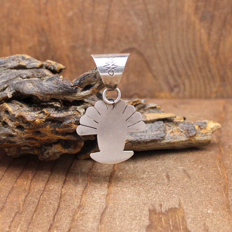 May include: Silver pendant in the shape of a stylized shell with a decorative bail. The pendant is made of sterling silver and has a smooth, polished finish.