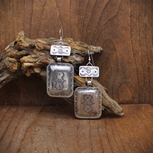 May include: A pair of silver dangle earrings with a geometric design. The earrings are made of two rectangular pieces, one smaller than the other, with intricate patterns.
