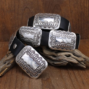 May include: A black leather belt with four silver belt buckles. Each buckle has a unique geometric design.