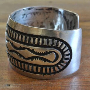 K&ouml;nnte beinhalten: Ein silbernes Armreif mit komplizierten geometrischen Mustern. Das Armband ist aus massivem Silber gefertigt und hat eine polierte Oberfl&auml;che.