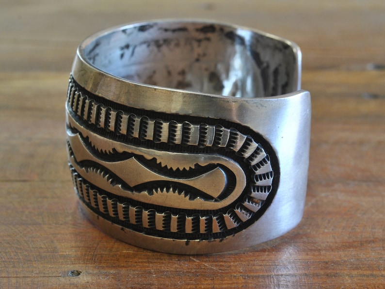 K&ouml;nnte beinhalten: Ein silbernes Armreif mit komplizierten geometrischen Mustern. Das Armband ist aus massivem Silber gefertigt und hat eine polierte Oberfl&auml;che.