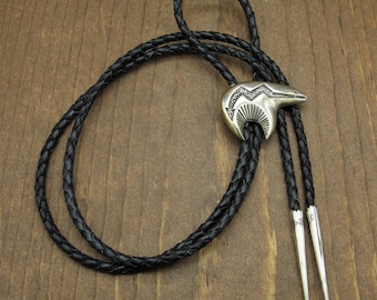 May include: A black leather bolo tie with a silver bear head pendant. The pendant has a detailed design and is accented with small silver dots.