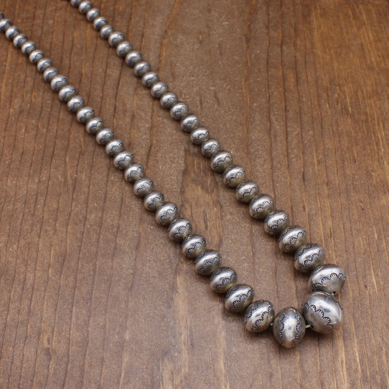 Puede incluir: Un collar de plata con cuentas redondas que tienen un dise&ntilde;o texturizado. El collar est&aacute; sobre una superficie de madera.