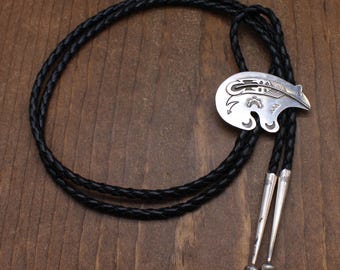 May include: A silver bolo tie featuring a bear design with intricate details. The tie is on a black leather cord.