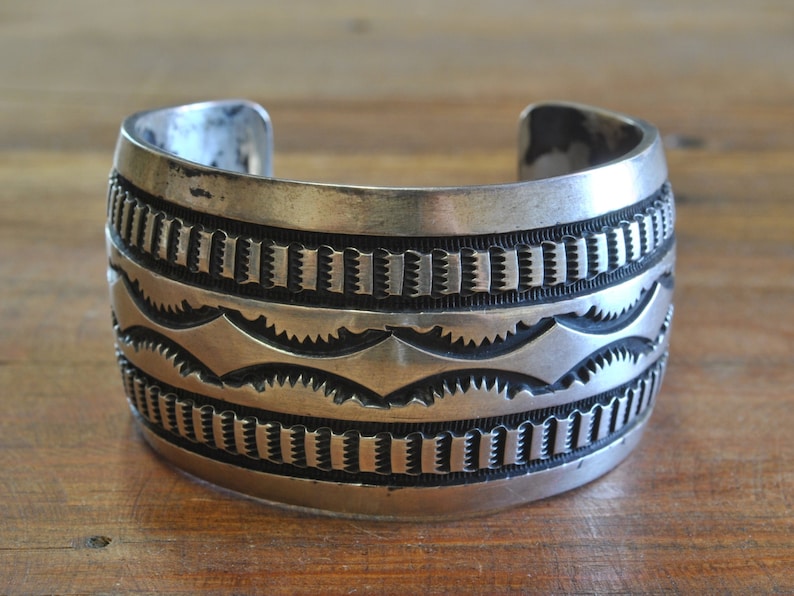 K&ouml;nnte beinhalten: Ein silbernes Armreif mit geometrischem Muster. Das Armband ist aus massivem Silber gefertigt und hat eine polierte Oberfl&auml;che.