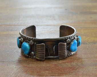 Può includere: Un braccialetto in argento con pietre turchesi. Il braccialetto presenta un design decorativo con una fascia in argento e una fila di pietre turchesi su ogni lato.