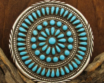 May include: A round silver and turquoise Native American belt buckle with a circular design of turquoise stones.