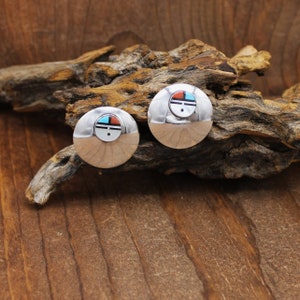 May include: A pair of silver earrings with a turquoise, red, and black geometric design. The earrings are round and have a smooth, polished finish.