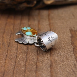 May include: Silver pendant featuring a turquoise stone set in a stylized wing design. The pendant has a decorative bail with a repeating pattern.
