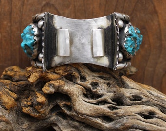 Könnte beinhalten: Ein silbernes Armband mit Türkis-Steinen, die in einer silbernen Fassung sitzen. Das Armband ist an der Rückseite offen und hat einen Scharnierverschluss.
