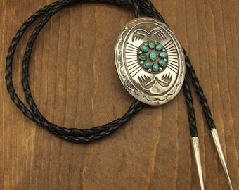 May include: A silver bolo tie with a turquoise stone inlay and a black braided cord.