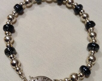 May include: A silver and black beaded bracelet with a silver clasp. The bracelet is made of round beads with alternating silver and black colors.