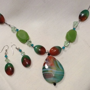 May include: A green, red and white agate stone necklace with matching earrings. The necklace features a large teardrop-shaped pendant and green and red oval beads.
