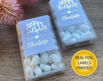 May include: Two clear plastic containers filled with white Tic Tacs. Each container has a purple label with silver foil lettering that reads "Happy Birthday Charlotte". The containers are on a wooden surface. The text "REAL FOIL LABELS PRINTED" is on a gold circle sticker.