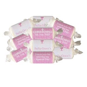 Peut inclure: Bo&icirc;tes de faveur roses et blanches avec un motif de croix et de calice. Les bo&icirc;tes indiquent "Bapt&ecirc;me" et "Bella-Grace's" avec la date "03 juillet 2022". Les bo&icirc;tes sont envelopp&eacute;es de cellophane transparent.