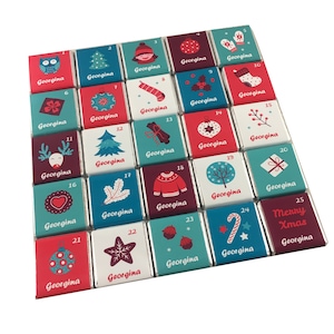 May include: A festive advent calendar with 25 chocolates, each individually wrapped. The wrappers are decorated with Christmas-themed illustrations, numbers, and the name "Georgina". Designs include a Christmas tree, owl, and a stocking.