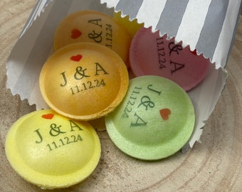 May include: A close-up of a paper bag filled with small, round, colorful candies. The candies are decorated with the letters "J & A" and the date "11.12.24".