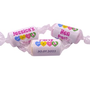 May include: Three pink and white wrapped candies with colorful hearts and the text "Jessica's Hen Party 30.07.2022" on one candy and "Hen Party" on another.