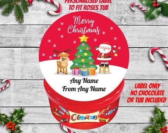 May include: A red and white round label with a Christmas theme. It features a cartoon Santa Claus, a reindeer, and a Christmas tree with presents. The label says "Merry Christmas" and has space for a name. The label is for a Roses chocolate tub.