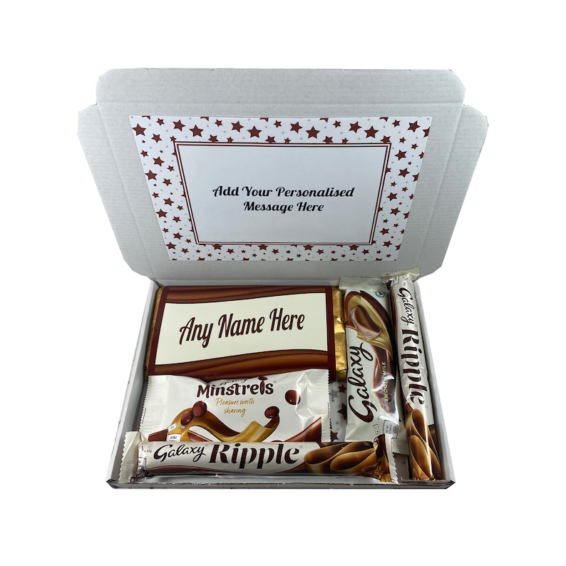 May include: A white cardboard gift box with a red star pattern on the lid. The box is open and contains a variety of chocolate bars, including Galaxy Ripple, Galaxy, and Minstrels. The box also includes a personalized message that says "Any Name Here".