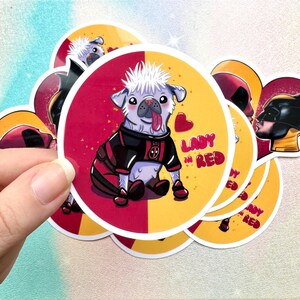May include: A circular sticker featuring a cartoon pug with spiky white hair and a tongue sticking out, wearing a black and red suit with a logo. The background is split between red and yellow, with a red heart and the text LADY IN RED.