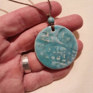 May include: A turquoise and white oval ceramic pendant with a brown cord necklace. The pendant has a marbled design.