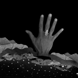 May include: A black and white image of a hand reaching up from a textured, mountainous landscape. The hand is wearing a silver ring with a geometric design.