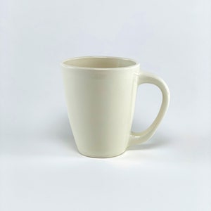 May include: A white ceramic mug with a handle. The mug is empty and has a smooth, rounded shape.