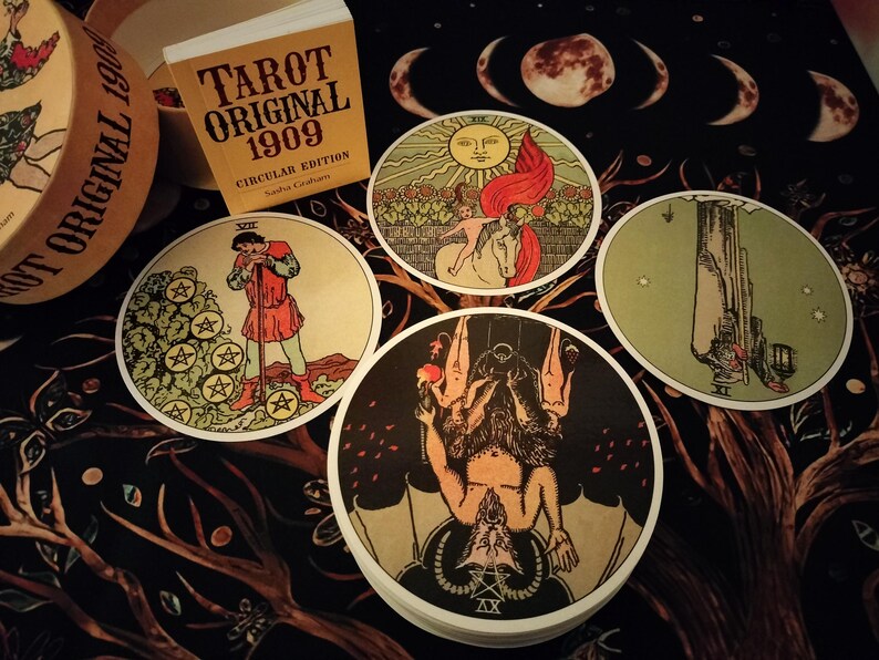 May include: Four tarot cards with circular white borders and colorful illustrations. The cards are laid out on a dark background with a pattern of branches and leaves. The cards depict the following: The Star, The Devil, The Hanged Man, and The Five of Pentacles. The cards are from the Tarot Original 1909 Circular Edition.