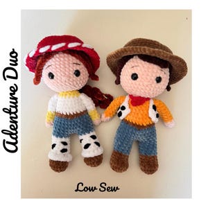 Op de afbeelding: Twee handgemaakte gehaakte poppen, een met een rode hoed en de andere met een bruine cowboyhoed. De poppen dragen outfits met een blauwe spijkerbroek en houden elkaars hand vast. De tekst "Adenture Duo" en "Low Sew" is zichtbaar.