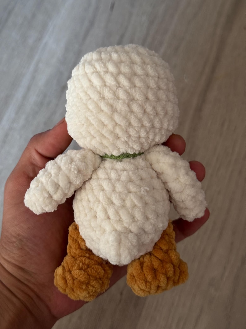 May include: A handmade, plush duck toy with a white body, brown feet, and a green neck band. The soft, textured material gives the duck a cuddly appearance. This adorable toy is perfect for children or as a decorative item.