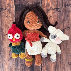 May include: A set of three handmade crochet plush toys including a doll with dark brown hair wearing a red top and white skirt, a red and green chicken with large white eyes, and a white pig with grey spots and a pink snout made of yarn.
