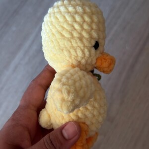 May include: A handmade, plush yellow duckling with an orange beak and feet. The duckling has small black eyes and a textured, soft appearance. The toy is likely crocheted or knitted, and is a cute, cuddly item.