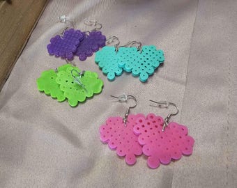 May include: A collection of handmade earrings in various colors, including purple, teal, green, and pink. Each pair features a cloud-like design with small, evenly spaced holes and silver-colored ear wires. The earrings are displayed on a neutral-toned fabric.