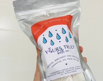 May include: A silver pouch with a white label that says "Wake Me Up Shower Steamer" and "Yours Truly bath co."  The label also includes a list of ingredients: Baking soda, citric acid, arrowroot powder, cream of tartar, essential oil, and witch hazel. The pouch contains 10 white shower steamers.