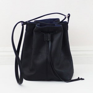 May include: A black leather bucket bag with a drawstring closure and a long strap.