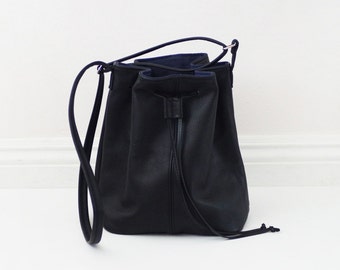 May include: A black leather bucket bag with a drawstring closure and a long strap.