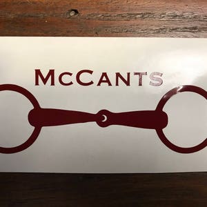 May include: A white sticker with a maroon horse bit silhouette and the text "MCCANTS" in maroon.