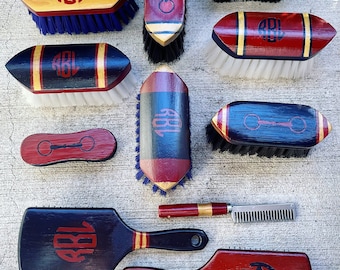 May include: A set of nine horse grooming brushes with various designs. The brushes are red, blue, black, and gold with the initials "RBL" on each. Some brushes have a horse bit design.