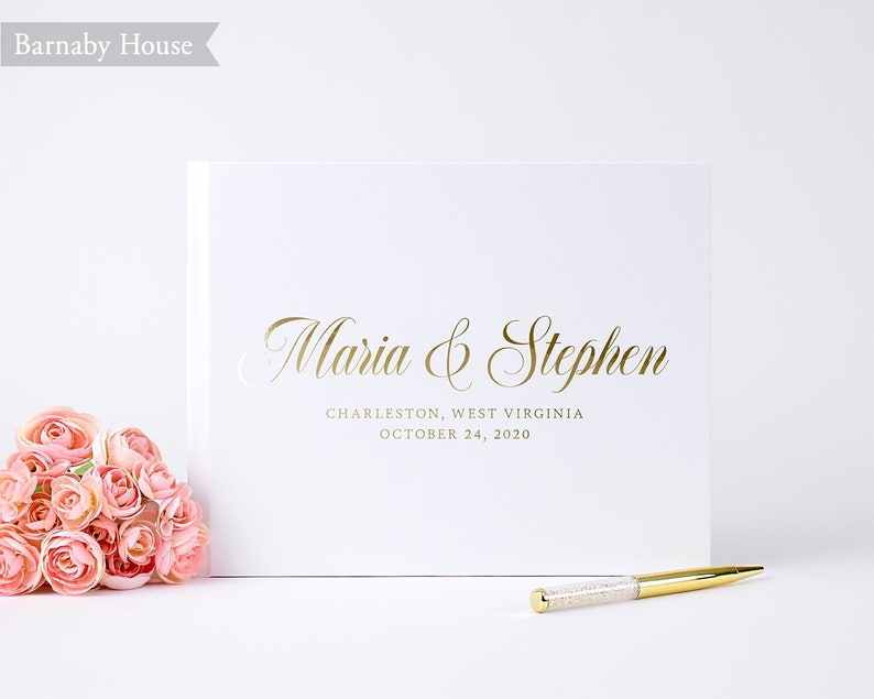 May include: White wedding guest book with gold foil lettering. The text reads "Maria & Stephen, Charleston, West Virginia, October 24, 2020".