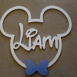 May include: White wooden Mickey Mouse head cutout with the name "Liam" in a stylized font and a blue bow tie.