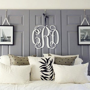 May include: A white bed with a gray headboard made of three repurposed doors. The headboard has two framed pictures of sailboats and a white wooden monogram in the center. The bed has white bedding and several decorative pillows.