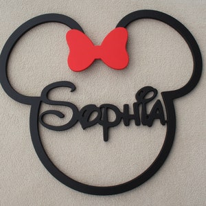 May include: Black wooden cutout of Mickey Mouse ears with a red bow and the name "Sophia" written in a stylized font.